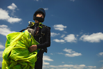 Skydiver figure with a parachute canopy in his hands after landing against the blue sky with...