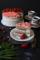 a piece of sponge creamy cake with strawberries on dark table with cups of coffee