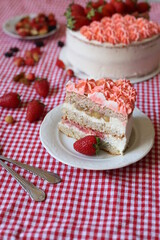 sponge creamy cake with strawberries on red checkered tablecloth