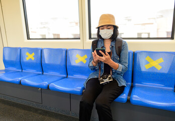 Asian woman sitting in the sky train keep social distancing from other people during covid-19