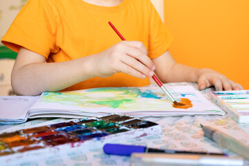 art painting, childrens hands holding brush and drawing of orange paint.
