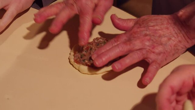 Grandmother senior hands preparing small pizza-like bread with ground beef topping, esfiha dish