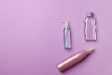 three different cosmetic bottles lying on purple colored paper background, with copy space