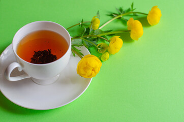 A Cup of black tea and yellow flowers of Trollius europaeus on a green background. Evening and morning tea. Copy space.