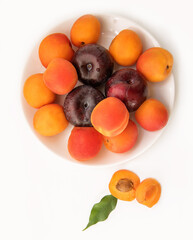 Juicy ripe apricots and plums with a green leaf on a plate close-up, on a white background