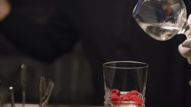 Making of hot sambuka with raspberries. Close up barmans hand sets fire to sambuca in snifter and pours it into a glass with raspberries. Then he covers it. Glass is slowly rotating