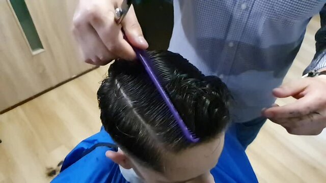 Haircut by the barber with scissors and comb in slow motion to a young person in a hair salon