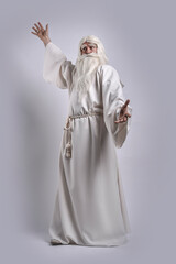 A grey-haired severe wizard in a white cassock is doing sorcery and magic against a gray background.