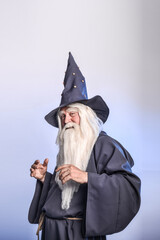 A severe grey-haired bearded sorcerer in a gray cassock and a cap is practicing sorcery and doing...