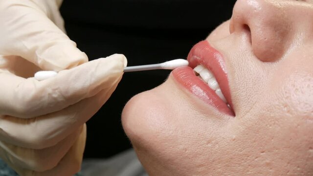 Beautician touches a cotton swab to permanent tattoo lip makeup. Light matte pink lips close up. Lips microblading procedure