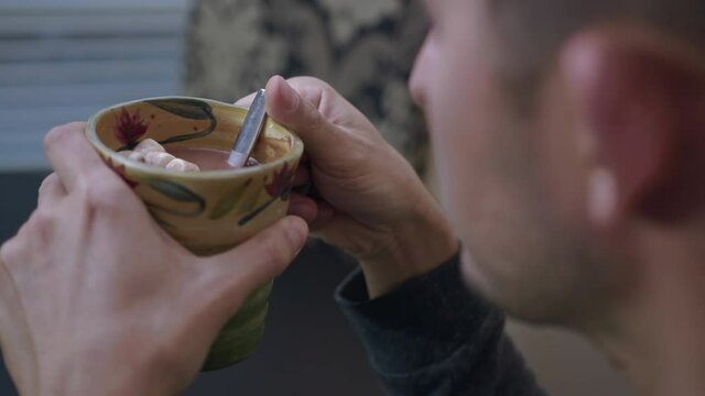 High quality close-up 4k slow motion video of a man mixing hot chocolate beverage in his cup with small white marshmallows view from the back. Handsome male drinking hot chocolate with marshmallows.