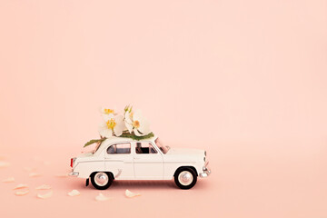 White retro toy car delivering flowers and gifts on a pink background. Copy space.