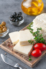 Adyghe cheese is cut into pieces. Cheese on a wooden board. Garnished with thyme, spices and cherry tomatoes. In the background olives and olive oil.