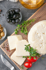 Cut Adyghe cheese into pieces. Cheese on a wooden board. Served with thyme, spices and cherry tomatoes.