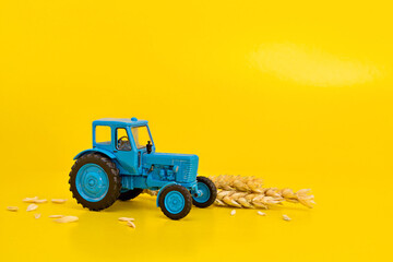Toy blue retro tractor collects a crop of wheat on a yellow background. Copy space.