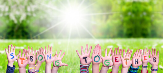 Children Hands Building Colorful Word Strong Together. Green Grass Meadow As Background