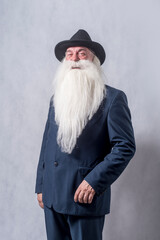 A grey-haired bearded old patriarch in a dark suit and a hat against a light background.