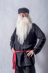 A grey-haired bearded old man, a patriarch in dark national clothes and boots against a light...