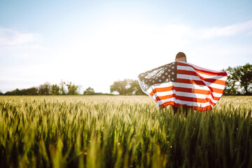 Young man proudly hold waving american USA flag. Patriot  raise national american flag against the blue sky. Independence Day, 4th July.