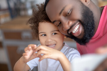 Sweet little girl showing love sign while her father making selfie