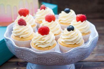 Vanilla cupcakes with cream cheese frosting and fresh berries, blueberry and strawberry. Rustic wooden background.