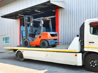 Red forklifts is parked on a tow truck parked in front of the warehouse.