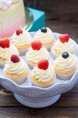 Vanilla cupcakes with cream cheese frosting and fresh berries, blueberry and strawberry. Rustic wooden background.