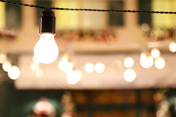 Glowing bulb on wire against blurred lights. Space for text