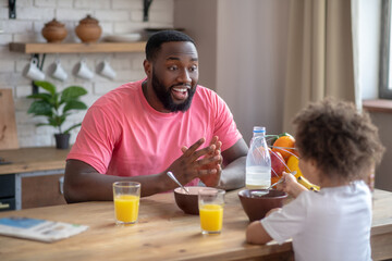 Fototapeta na wymiar African american man in a pink tshirt and his daughter having breakfast