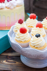 Vanilla cupcakes with cream cheese frosting and fresh berries, blueberry and strawberry. Rustic...