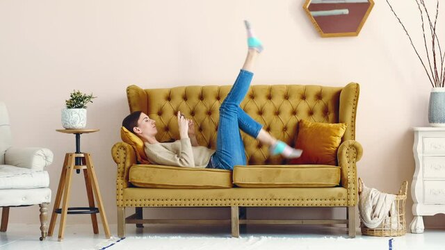 Girl lies on the couch holding smartphone watching movie and  dangles legs