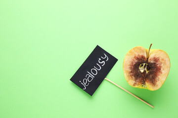 Rotten apple and JEALOUSY sign on green background, flat lay. Space for text