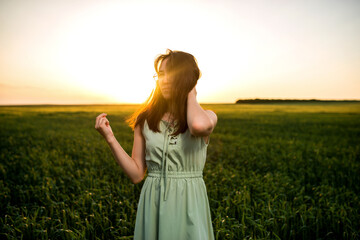 Obraz premium young, beautiful Asian girl in a field of green wheat on the background of the sunset