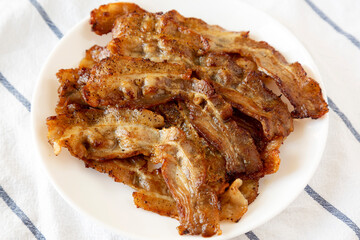 Homemade Fried Bacon on a white plate on cloth, low angle view. Close-up.