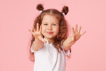 Portrait of surprised cute little toddler girl child over pink background. Looking at camera. Points hands to the left side. Advertising childrens products