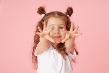 Portrait of surprised cute little toddler girl child over pink background. Looking at camera. Points hands to the left side. Advertising childrens products