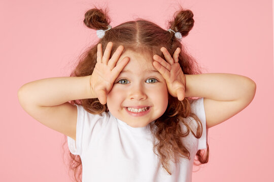 Portrait of surprised cute little toddler girl child over pink background. Looking at camera. Points hands to the left side. Advertising childrens products
