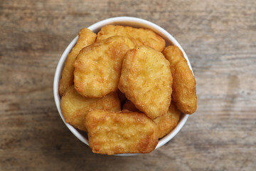 Bucket with tasty chicken nuggets on wooden table, top view