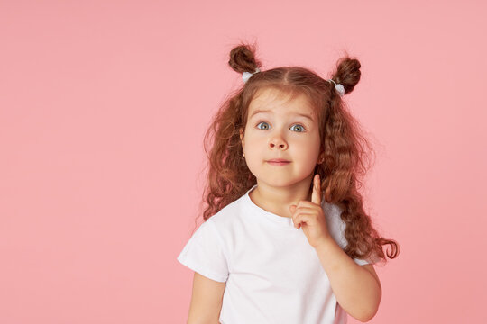 Naklejki Portrait of surprised cute little toddler girl child over pink background. Looking at camera. Points hands to the left side. Advertising childrens products