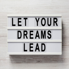 'Let your dreams lead' on a lightbox on a white wooden background, top view. Flat lay, from above, overhead.