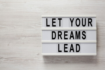 'Let your dreams lead' on a lightbox on a white wooden background, view from above. Flat lay, top view, overhead.