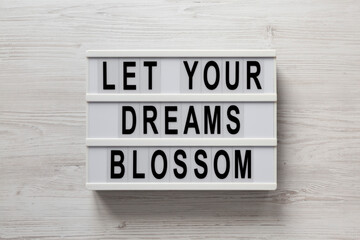 'Let your dreams blossom' on a lightbox on a white wooden background, top view. Flat lay, overhead, from above.
