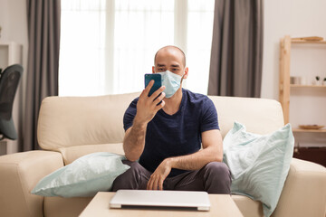 Man watching a video on smartphone wearing protection man while sitting on sofa during quarantine.