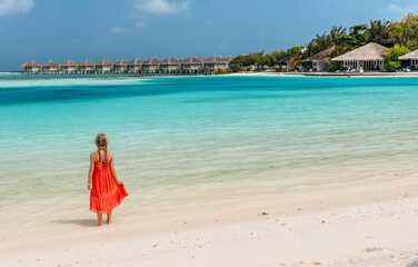 Fototapeta na wymiar Girl in a red dress on the beach in Maldives.