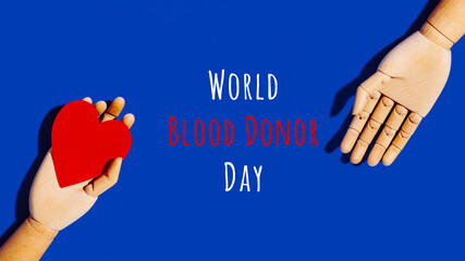 Wooden hand with big red heart in a giving gesture. World Blood Donor Day wording. Donation, help, health issues, antibody plazma concepts. Banner format - obrazy, fototapety, plakaty