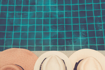 Straw hats at the pool edge with palm reflections in the water. Relax vacation, sun protection, travel fashion concept