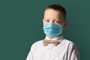 School boy wearing face mask standing against blackboard. Safe back to school during pandemic...