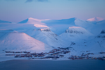 View over Longyearbyen and the snow covered mountains with pink light in March