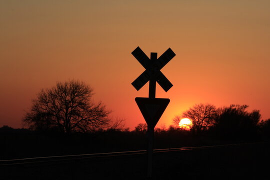 railroad crossing sign at sunset with silhouettes in Kansas.