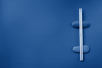 Flat lay. Light wooden chopsticks lie on oval stones on a pink background. Traditional Asian cutlery. Copy space